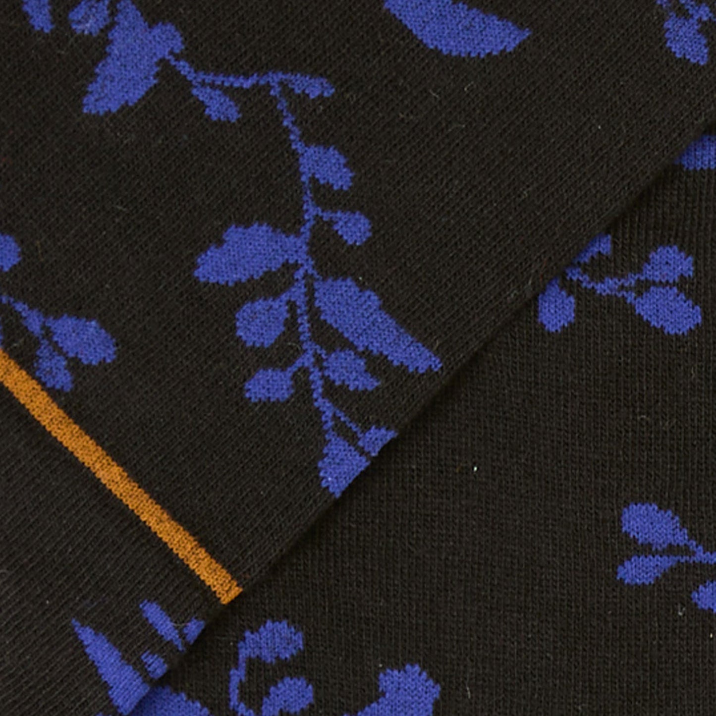 Dettaglio floreale dei calzini lunghi a fiori di Arturo Stories, con fondo nero e decorazioni blu e senape.