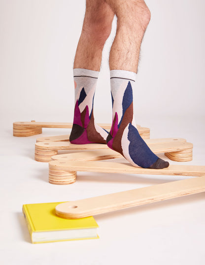 Calze "Svetta in alto" lunghi da uomo di Arturo Stories. Montagne e sole ricamati su fondo grigio chiaro.